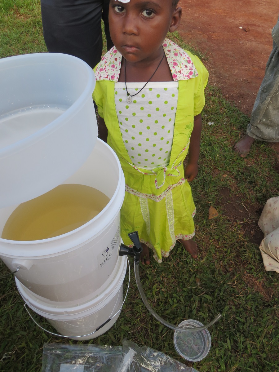 The water in the filter is a brown color, while the water in the clear container on the ground is clean and clear. Daniella, looking on, is another of Angela's grandchildren. Kollin gave her a gift of a new dress. Thanks to her sponsor, Toni G., she is able to attend Baby Class at St. Anthony Nursery School.